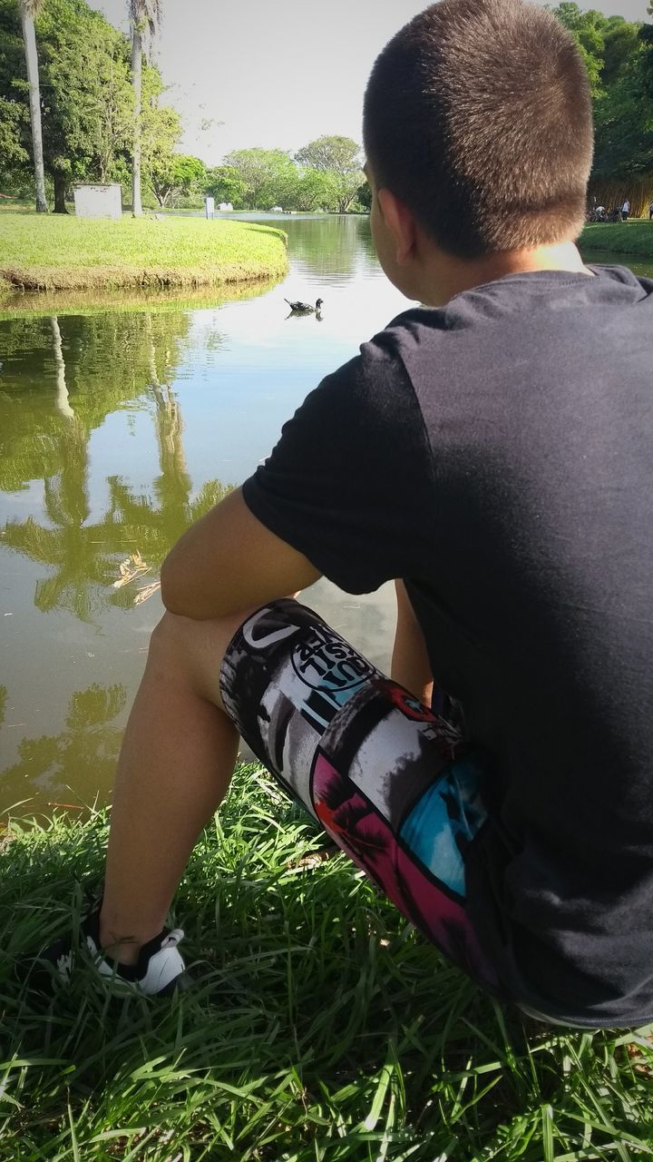 REAR VIEW OF BOY SITTING AT LAKE