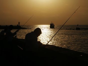 Silhouette men fishing in sea against sky during sunset