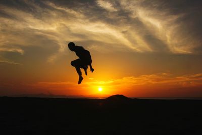 Silhouette man jumping against orange sky during sunset