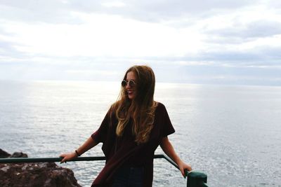 Young woman leaning on railing against sea