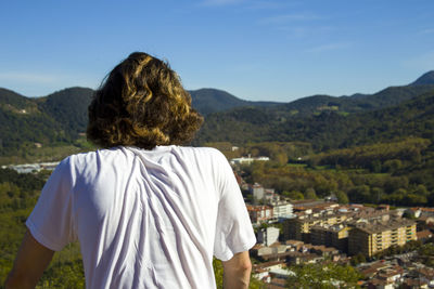 Rear view of hiker standing against town on sunny day