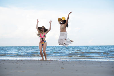 Cheerful female friends wearing swimwear at beach against cloudy sky
