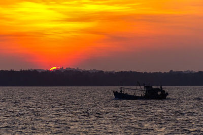 Silhouette boat in sea against orange sky