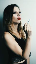 Young woman smoking cigarette while standing by wall