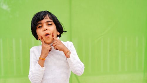 Asian little girl pointing finger to her chick on isolated green background. facial and skin care co