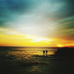 Silhouette people on beach against sky during sunset