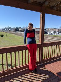 Full length portrait of smiling standing on railing against sky