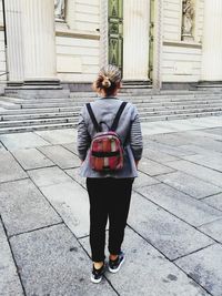 Rear view of woman standing on footpath against building