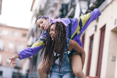 Low angle view of happy woman piggybacking female friend in city