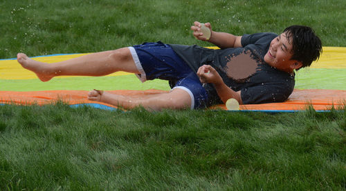 Cheerful boy holding water balloons while lying on field at park