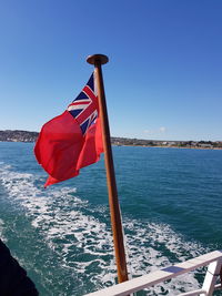 Red flag by sea against clear blue sky