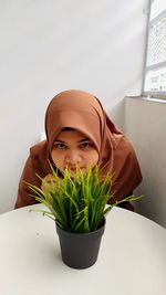 Portrait of young woman against potted plant against wall