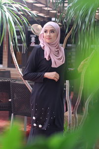 Portrait of young woman standing against plants