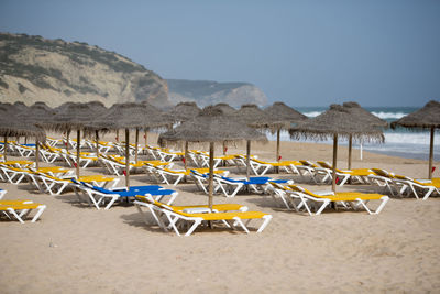 Deck chairs on sand at beach against clear sky