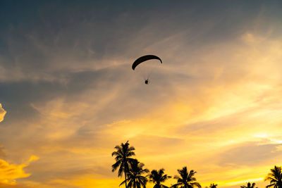 Low angle view of people paragliding against sky during sunset