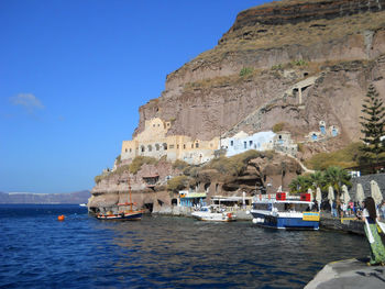 Boats in sea by buildings against clear blue sky