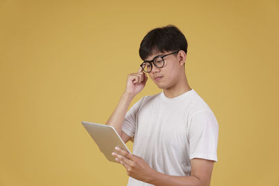 Midsection of man using smart phone against yellow background