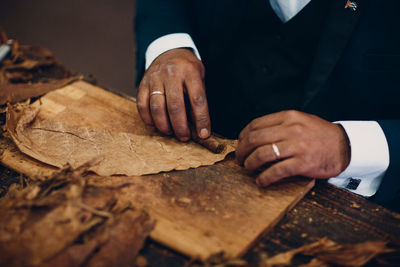 Close-up of man wearing suit making cigar at table