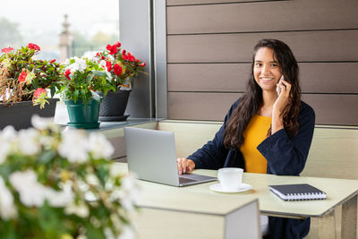 Hispanic freelancer using laptop and speaking on cellphone