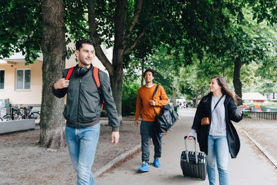 Young friends walking on street with luggage in city