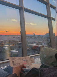 Man holding glass window against sky at sunset