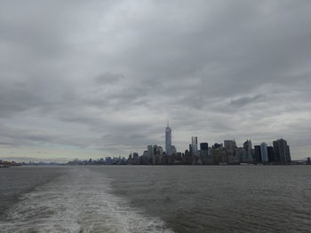 Sea and buildings in city against cloudy sky