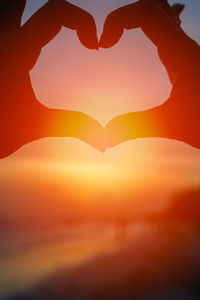 Silhouette of heart shape against orange sky