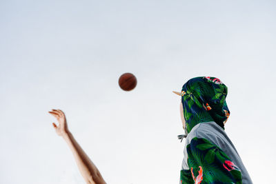 Low angle view of man looking at basketball in mid-air against clear sky