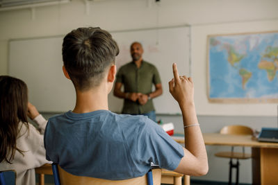 Teenage boy student pointing while male professor teaching in high school