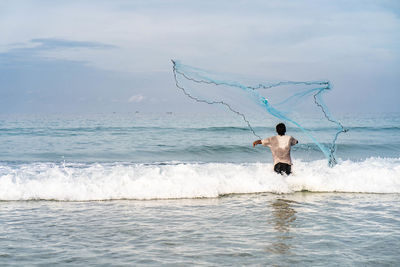 Full length of shirtless man in sea against sky