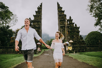 Couple running on footpath at gate against sky