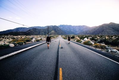 Rear view of men walking on road against mountain range