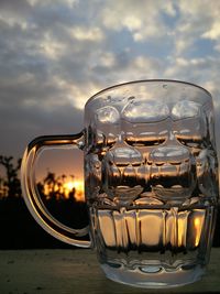 Close-up of glass on table against sky during sunset