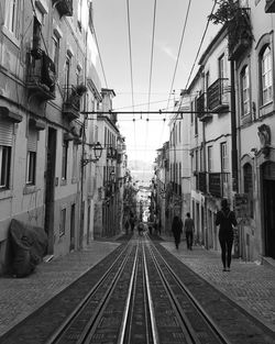 People on railroad tracks in city against clear sky