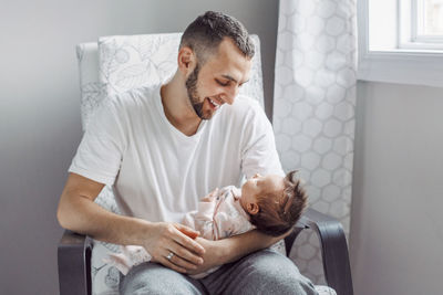 Smiling man holding baby girl while sitting on chair at home