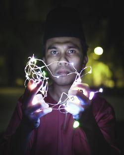 Portrait of man holding string lights at night