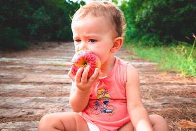 Cute girl eating apple while sitting on dirt road