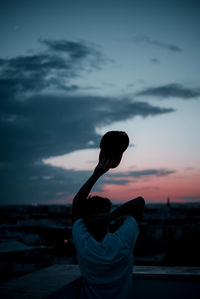 Rear view of man standing at beach against sky during sunset