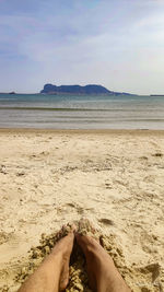 Low section of person on beach against sky