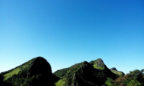 Low angle view of rocky mountains against clear blue sky