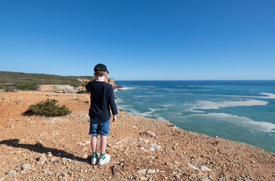 Young boy standing on a coastal footpath looking out to sea