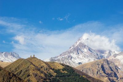 Scenic view of tiny monastery located on the top of the hill against snowcapped mountains anblue sky