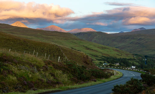 Road amidst green landscape against sky during sunset