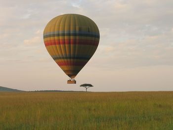 Hot air balloon over grassy field against sky