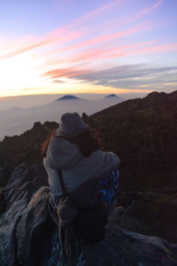 Man sitting on rock against sky during sunset