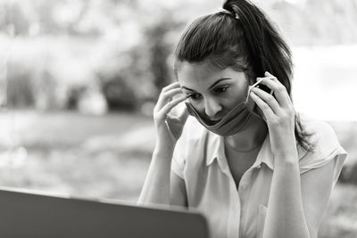 Woman wearing mask while looking at laptop at park