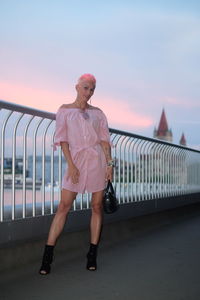 Full length of woman standing on railing against sky during sunset