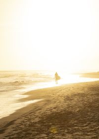 Silhouette woman walking at beach against sky during sunset