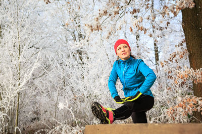 Low angle view of mid adult woman exercising in forest during winter