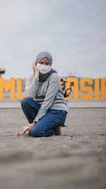 Full length of young woman sitting on mobile phone against sky